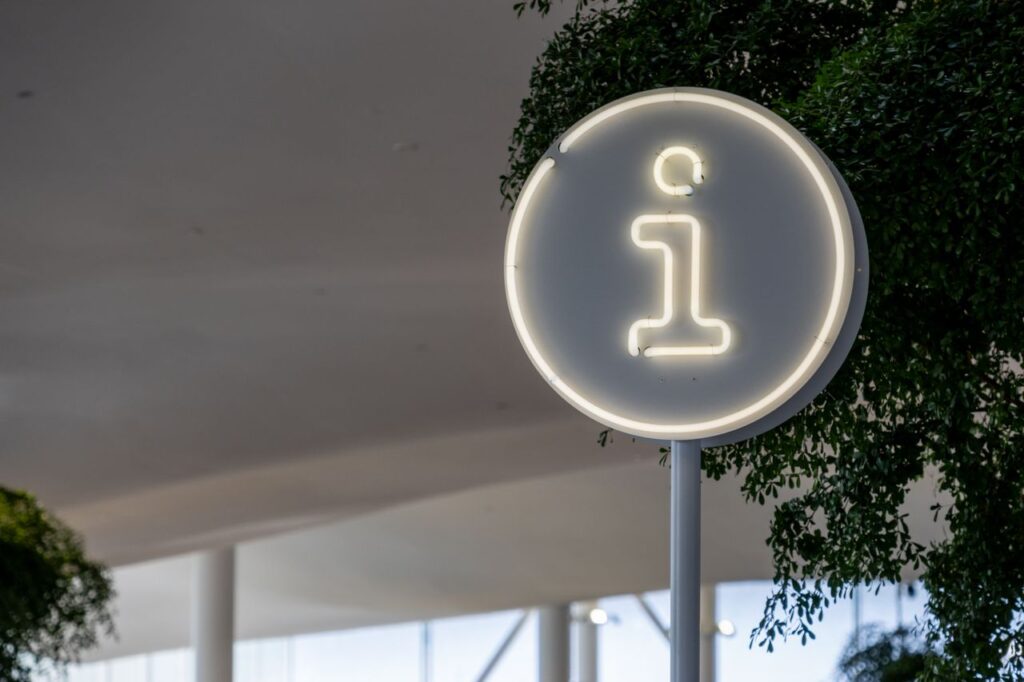 Modern info sign at Helsinki library with minimalist design and foliage.